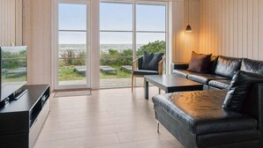 A modern living room with a large sliding glass door leading to a balcony with a view of the sea. - 4 Star Holiday Home in Nexo (Nexø)