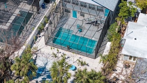 A rooftop swimming pool with a glass enclosure, surrounded by trees and a building with a sloped roof. - The Pelican on Siesta (Siesta Key)