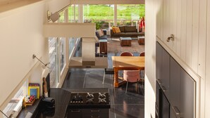 A modern kitchen with a gas stove, a dining area with a wooden table and chairs, and a view of a green garden through large windows. - Luxe Villa With Pool and Sauna in Spijkerboor (Spijkerboor)
