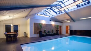 An indoor swimming pool with a skylight ceiling, a dining area with a table and chairs, and a wall-mounted planter with plants. - Luxe Villa With Pool and Sauna in Spijkerboor (Spijkerboor)