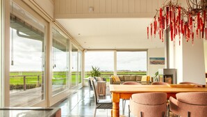 A spacious dining area with a large table and chairs, large windows offering a view of the countryside, and a modern chandelier. - Luxe Villa With Pool and Sauna in Spijkerboor (Spijkerboor)