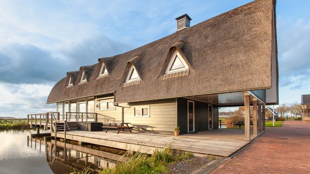 A modern building with a sloped roof, a dock, and a calm water body in the foreground. - Luxe Villa With Pool and Sauna in Spijkerboor (Spijkerboor)