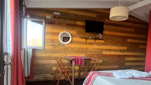 Una habitación acogedora con techo de madera, una cama, una mesa con sillas, un televisor y una ventana con cortinas.