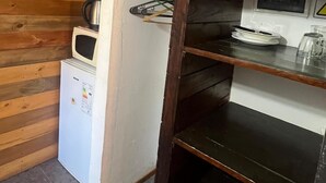 Cocina compacta con pared de madera, refrigerador blanco, microondas y repisas con vajilla.