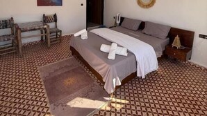 A bedroom with a bed, a bench, a painting, and a patterned floor.