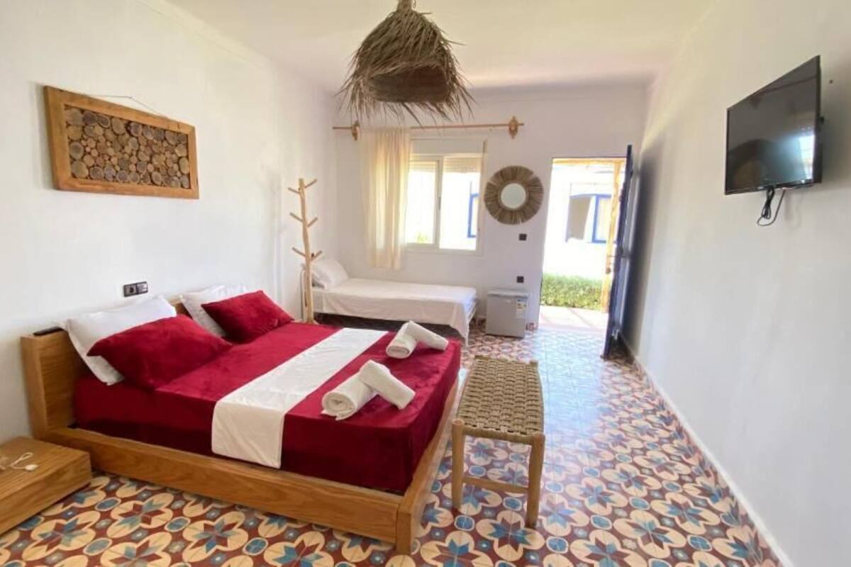 Ein Schlafzimmer mit einem hölzernen Bett, einem kleinen Nachttisch, einem an der Wand befestigten Fernseher und einem gemusterten Boden.
