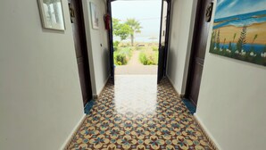 A hallway with patterned floor tiles, a painting of a beach scene, and a door leading to an outdoor area with a view of the sea.