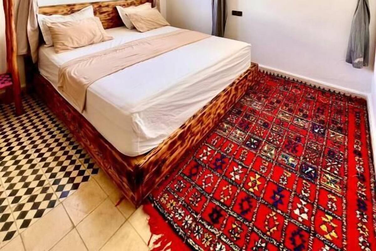 Ein Schlafzimmer mit einem Bett, Vorhängen, einem Fenster und einem gemusterten Teppich.