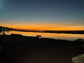Sonnenuntergang über ruhigem Gewässer mit Steg und kleinem Boot.