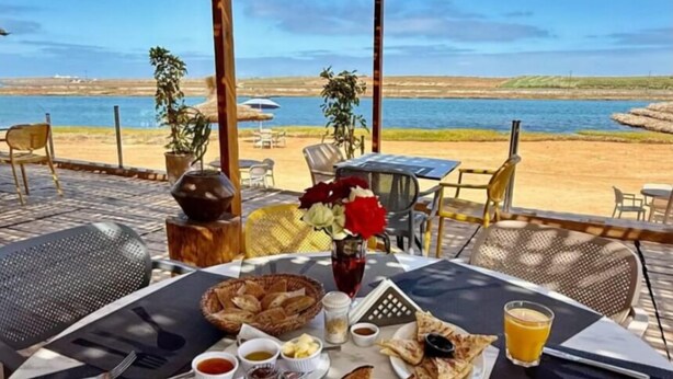 A breakfast table with various dishes and drinks, overlooking a beach and sea.