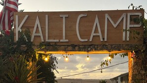 A wooden sign with "KALICAMP" written on it, leading to a pathway with potted plants and string lights.