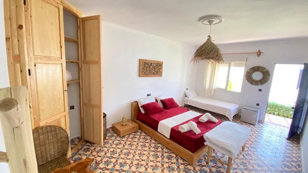 A bedroom with a bed, a wooden wardrobe, a wicker chair, and a patterned floor.