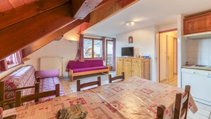 A cozy room with a wooden ceiling, a sofa, a dining table, a TV, and a kitchen area. - Apartment "Le Ressoutan" with Mountain View and Balcony (Saint-Colomban-des-Villards)