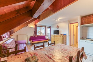 Een gezellige kamer met houten plafond, een bank, een eettafel, een televisie en een keukenhoek.