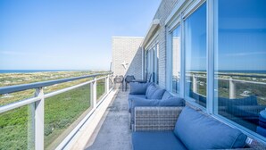 A balcony with a view of the ocean, a seating area with cushions, and a table with chairs.