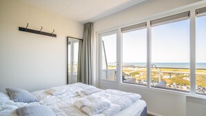 A bedroom with a large bed, a window with a view of the beach, and a coat rack on the wall.