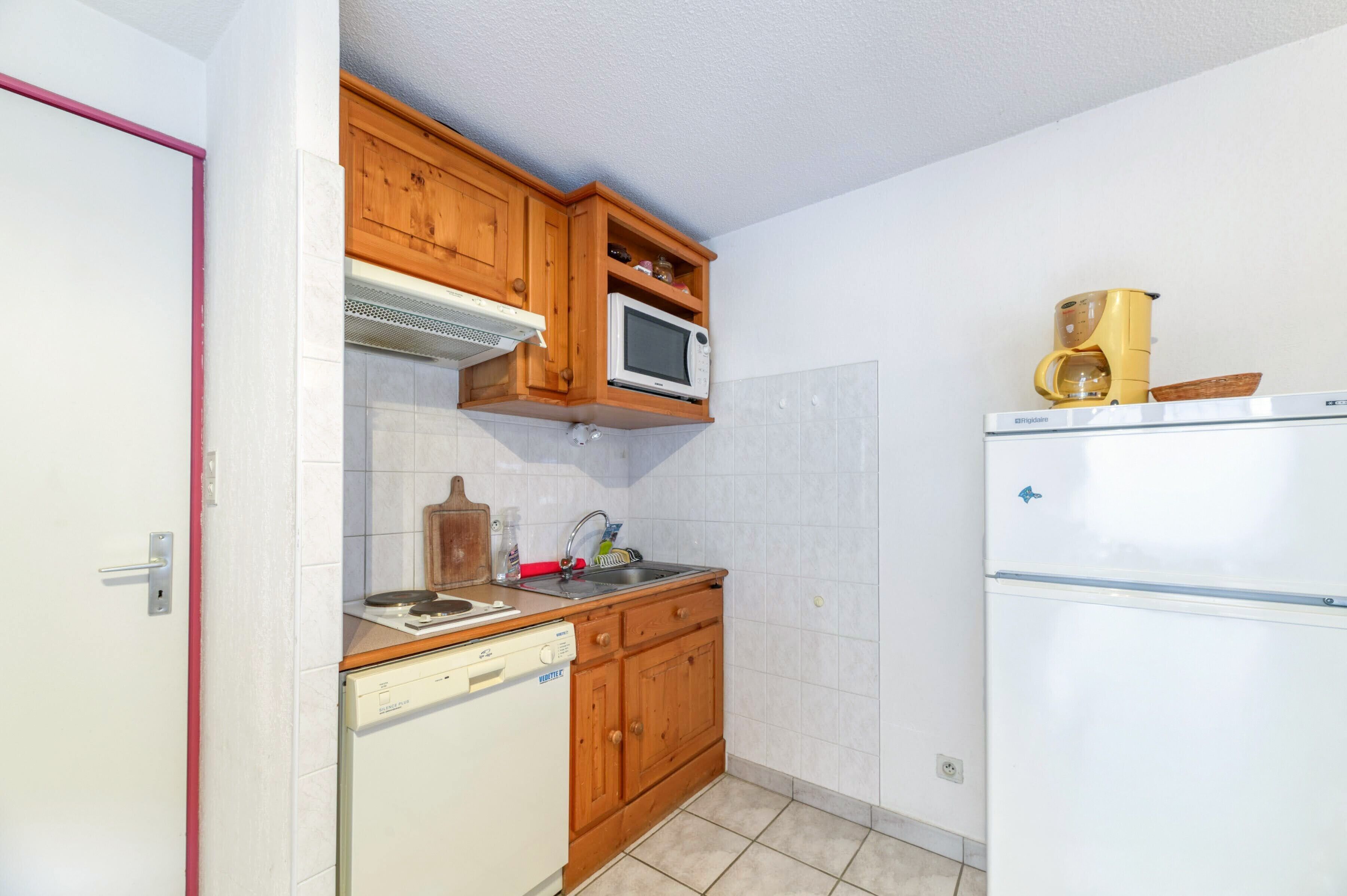 A compact kitchen with wooden cabinets, a microwave, a coffee maker, and a dishwasher.