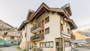 A multi-story building with balconies, a shop on the ground floor, and a mountainous backdrop.