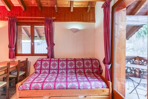 Un lit en bois avec une couvre-lit à motifs, une table en bois et des chaises, ainsi qu’une fenêtre avec des rideaux.