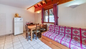 Une cuisine de taille réduite comprenant une table et des chaises, un canapé recouvert d’un tissu à motifs et un réfrigérateur.