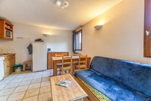 A compact kitchen with a dining area, a sofa, and a small table with a magazine.
