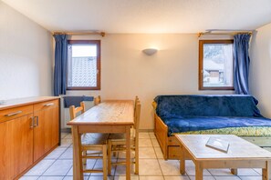 A compact room with a wooden table, a sofa, a cabinet, and two windows with curtains.