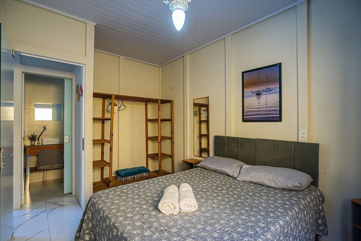 A bedroom with a bed, a wardrobe, a mirror, and a painting of a sailboat.