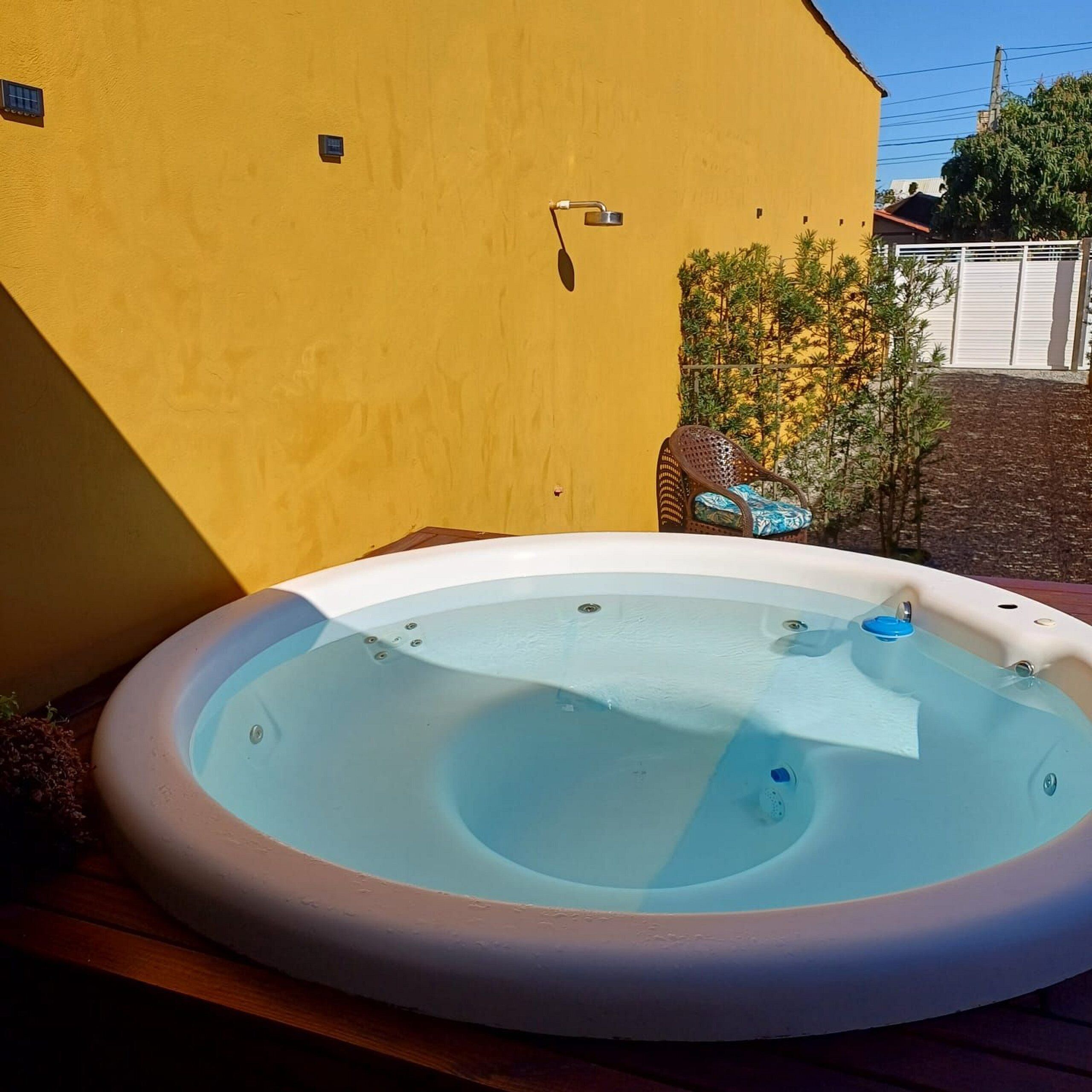 Un jacuzzi dans un jardin, avec un mur jaune et un petit arbre.