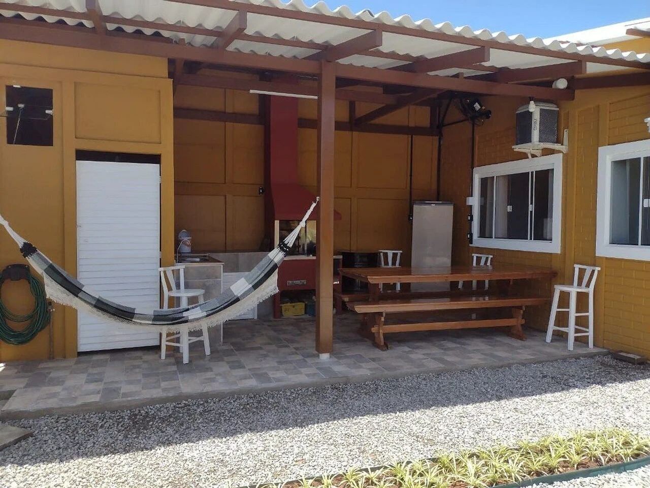 Un patio exterior techado con una hamaca, bancos de madera y una mesa.
