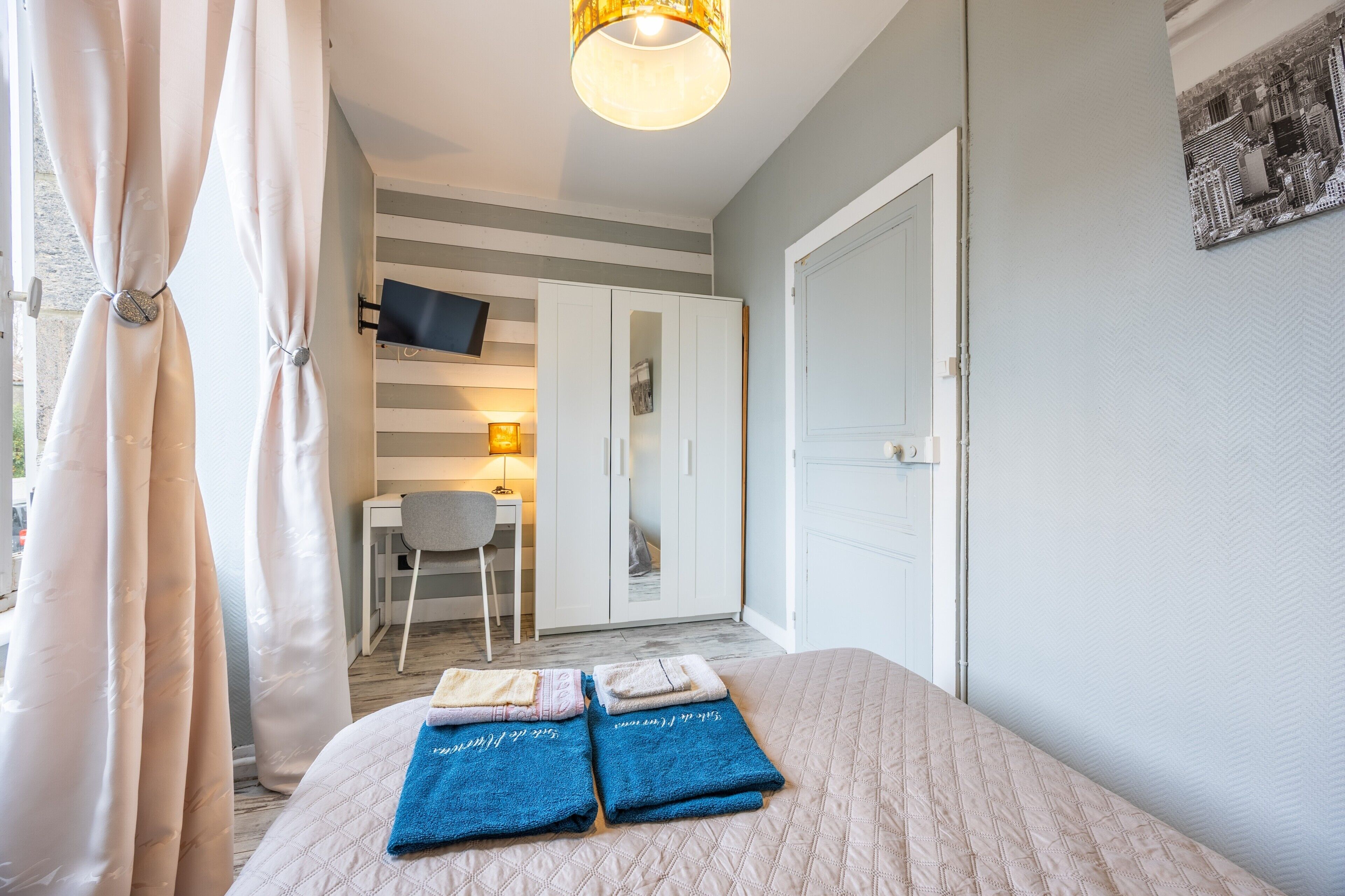 A bedroom with a bed, a desk, a chair, and a TV mounted on the wall.