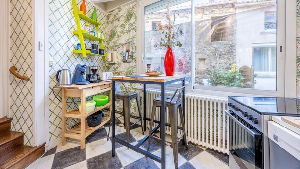 Une cuisine avec une fenêtre, un radiateur, une cuisinière et une table en bois avec des chaises.