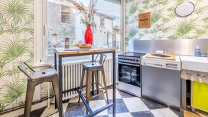 Une cuisine avec une fenêtre, un vase rouge, une horloge et un radiateur.