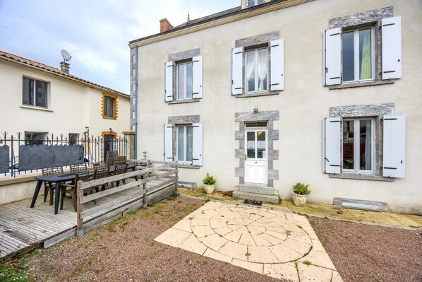 Un bâtiment à deux étages avec une cour, un banc en bois et une petite table.