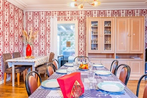 A dining area with a table set for four, chairs, a vase with dried flowers, and a cabinet with glassware.