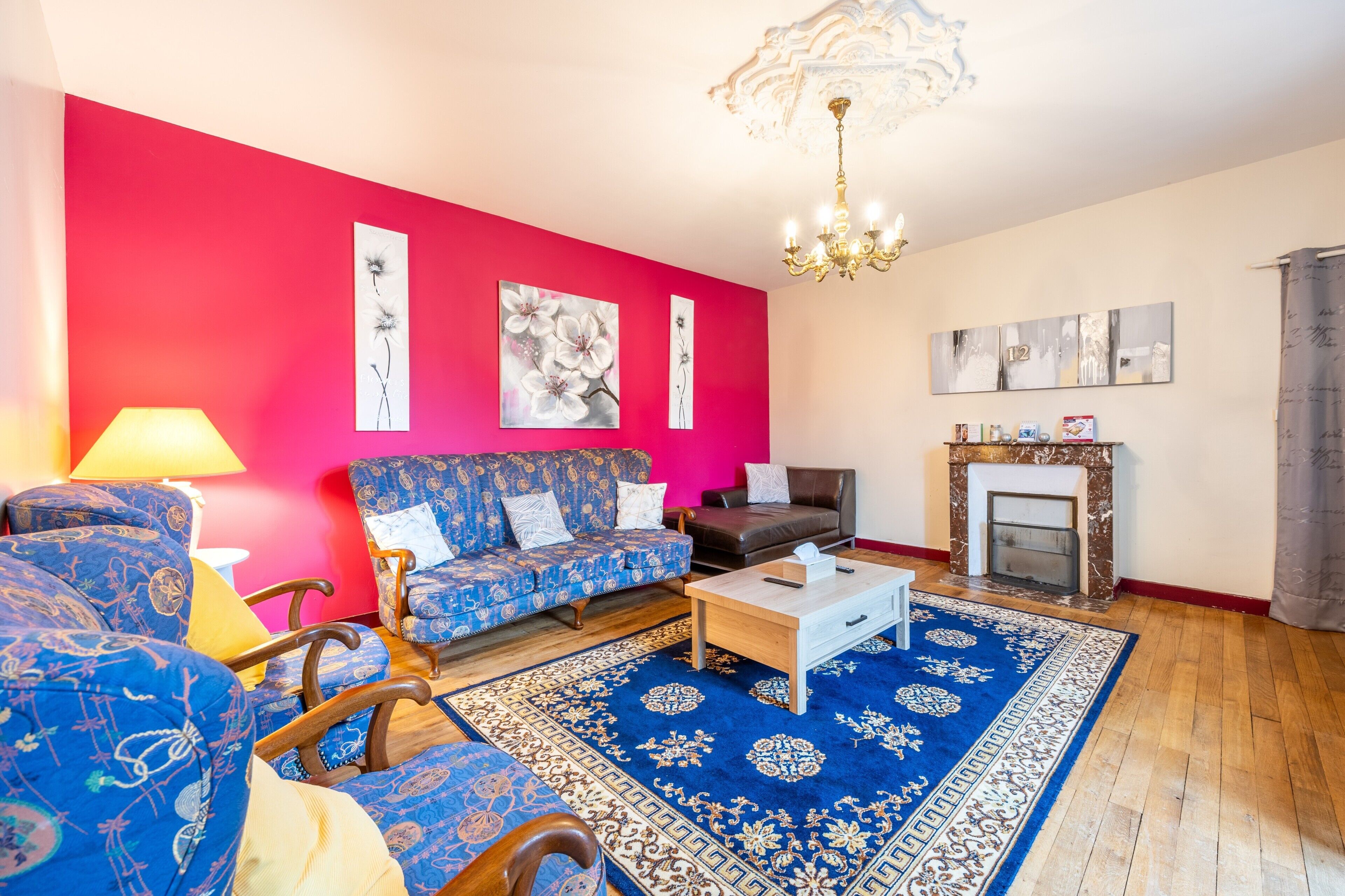 A living room with a red wall, blue patterned sofa, a wooden coffee table, and a fireplace.