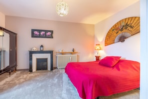 A bedroom with a bed, a fireplace, a radiator, and a wall-mounted fan.