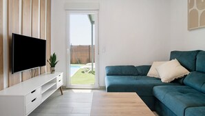 A living room with a flat-screen TV, a teal sofa, and a wooden TV stand. - Holiday Home 'Casita Perla' with Private Pool, Wi-Fi and Air Conditioning (Conil de la Frontera)