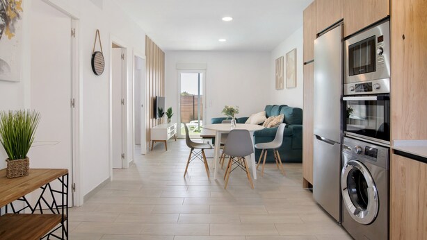 A modern kitchen with a built-in oven and microwave, a dining area with a round table and chairs, and a living area with a sofa and a plant. - Holiday Home 'Casita Perla' with Private Pool, Wi-Fi and Air Conditioning (Conil de la Frontera)