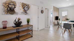 A modern living room with a dining area, featuring artwork on the walls, a wooden console table, and a view through an open door. - Holiday Home 'Casita Perla' with Private Pool, Wi-Fi and Air Conditioning (Conil de la Frontera)