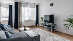 A modern living room with a grey sofa, a round coffee table, a flat-screen TV on a stand, and a large window with curtains. - Spacious City Retreat with Private Sauna (Helsinki)