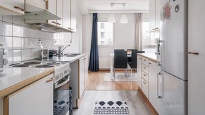 A modern kitchen with white cabinets, a stove, and a dining area with a table and chairs. - Spacious City Retreat with Private Sauna (Helsinki)