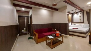 A hotel room with a bed, a red sofa, a coffee table, and a ceiling fan. - Ananya Hotel  (Digha)