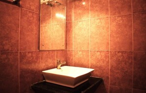 A bathroom with a white sink, a mirror, and brown tiled walls. - Ananya Hotel  (Digha)