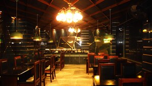 A restaurant interior with wooden tables and chairs, a central bar, and pendant lighting. - Ananya Hotel  (Digha)