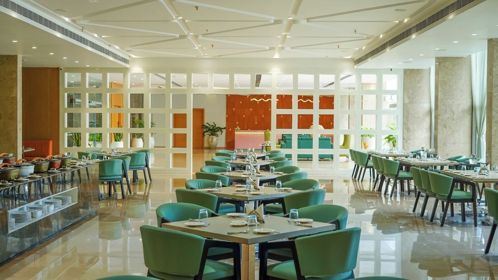 A spacious dining area with multiple tables and chairs, a buffet counter, and a large windowed wall providing natural light.