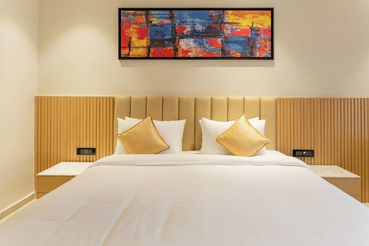 A hotel room with a large bed, two nightstands, a wooden headboard, and a colorful abstract painting on the wall.