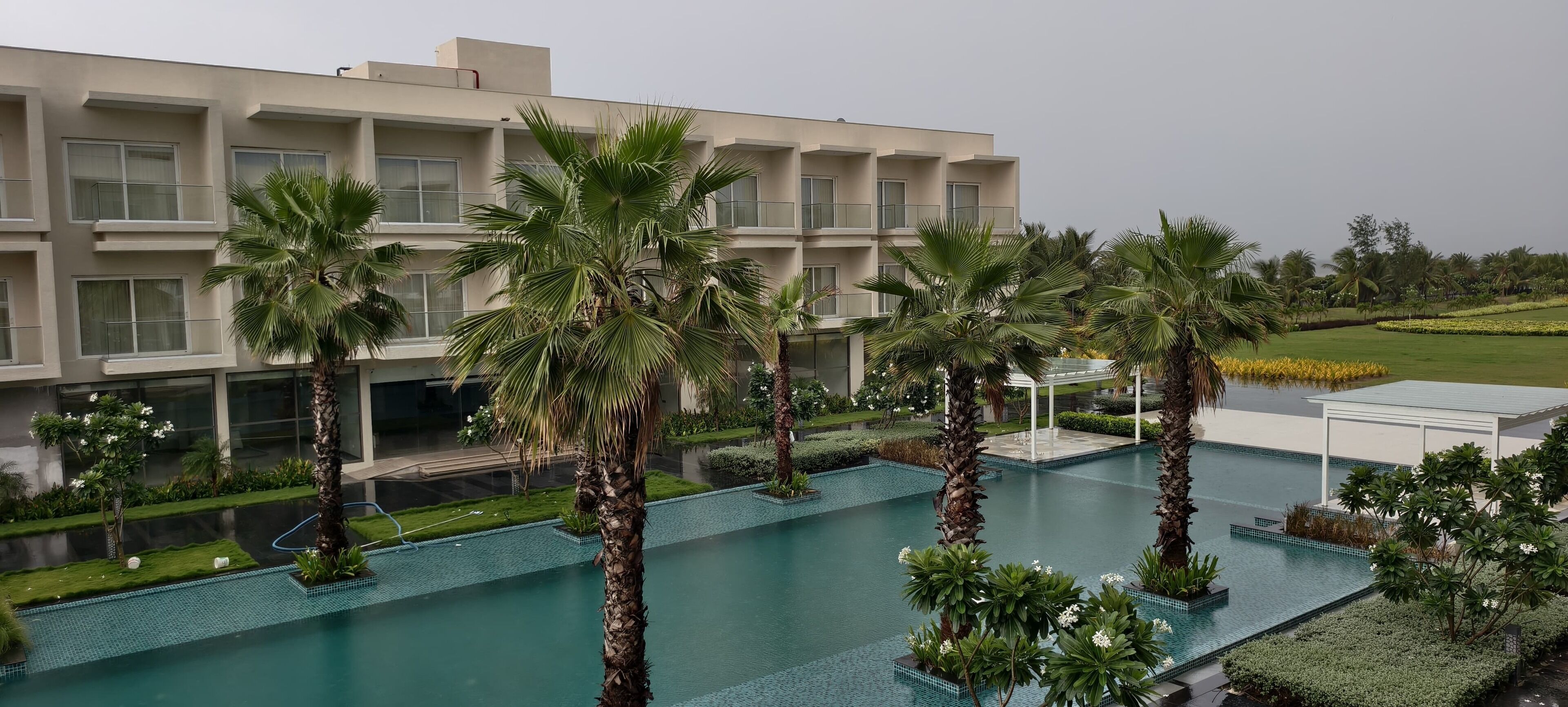 A modern building with a pool area, surrounded by palm trees and well-maintained landscaping.