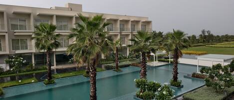 A modern building with a pool area, surrounded by palm trees and well-maintained landscaping.