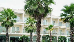 A hotel with multiple balconies, a swimming pool, and palm trees. - Golden Sands - By The Bay Resorts (Bapatla)