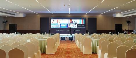 A conference room with rows of white chairs, a large screen at the front, and a carpeted floor.